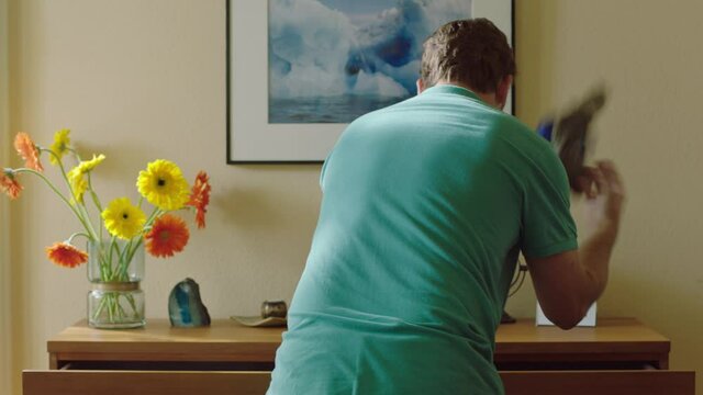 A man standing at his dresser, opening the drawers and throwing clothes out, looking for something