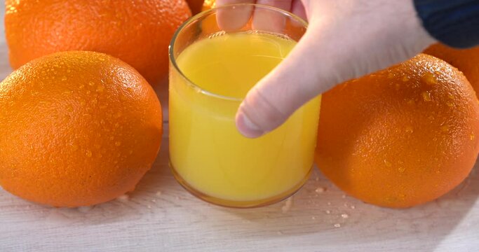 Man's hand takes the glass of orange juce from the white table