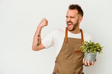 Young gardener tattooed caucasian man holding a plant isolated on white background raising fist...