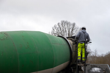 Man worker on a ladder checking concrete mixer truck. Construction worker in housing development.