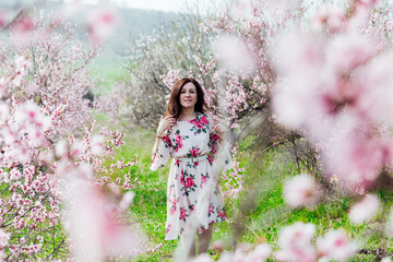 Beautiful woman in a dress with flowers walks through the flowering garden in spring