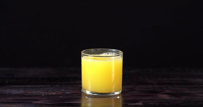 Orange juce is pouring to the empty glass on the black background