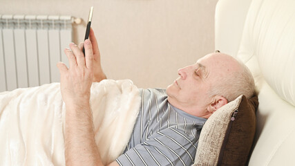 Lonely elderly man with tablet on bed