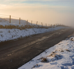 A deep fog rises over an icy country road during sunset in the middle of winter