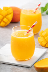 Fresh mango juice smoothie in a glass cup on gray table background.