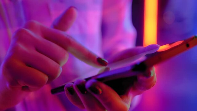 Woman using smartphone device at interactive exhibition or museum with purple illumination - scrolling and touching - close up view. Futuristic, retrowave, immersive, entertainment concept