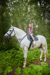 A teenage girl and a horse in nature among green trees