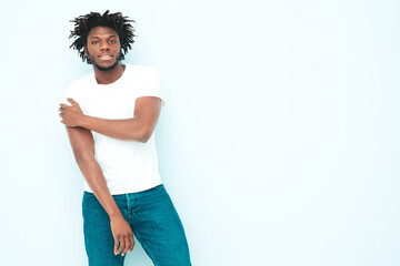 Portrait of handsome smiling hipster lambersexual model.Unshaven African man dressed in summer stylish clothes. Fashion male with dreadlocks hairstyle posing near light blue wall in studio