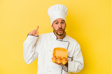 Young caucasian chef man holding eggs isolated on yellow background having some great idea, concept of creativity.