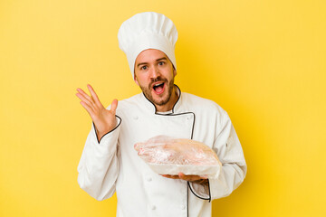 Young caucasian chef man holding chicken isolated on yellow background surprised and shocked.
