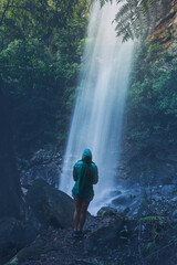 Woman hiker standing below a waterfall after rain