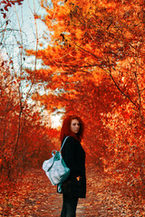 Red-haired woman walks in the forest in autumn with blue blackpack