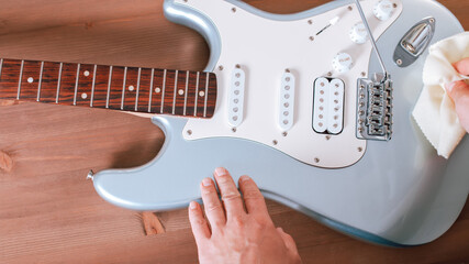 Guitar master polishing and restringing electric guitar, top view, closeup