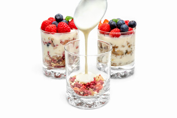 Muesli with yogurt and berries in a glass On a white background. Yogurt is poured from a spoon into a glass. Dessert preparation process. Healthy breakfast. Fitness food. High quality photo