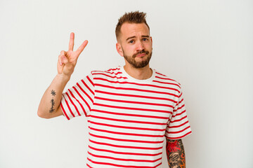 Naklejka premium Young tattooed caucasian man isolated on white background joyful and carefree showing a peace symbol with fingers.