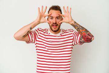 Young tattooed caucasian man isolated on white background keeping eyes opened to find a success opportunity.
