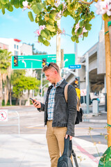 A young man in a denim jacket uses a smartphone while standing on a Los Angeles street next to a...