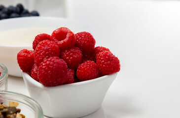 Raspberries in a white vase on a white table. Ingredients for dessert. Copy space. High quality photo