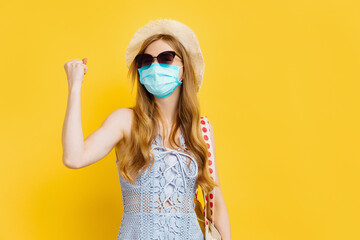 happy young woman in medical mask and summer hat, rejoicing at her success and victory, clenching her fists for joy on a yellow background