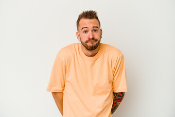 Young tattooed caucasian man isolated on white background shrugs shoulders and open eyes confused.