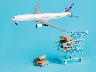 Plane flies around the shopping trolley and cardboard boxes on blue background. Creative cargo delivery by air concept. Free and fast freight global transportation.