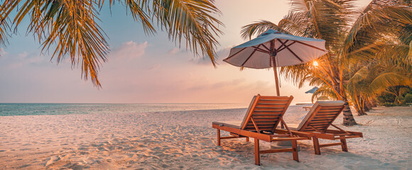 Luxury panoramic tropical sunset beach banner. Two sun beds loungers, umbrella under palm tree....
