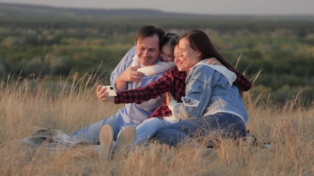 Happy family and smartphone. Dad, Mom, happy children are photographed on smartphone in park. Parents and daughters take selfies while traveling in nature. Cheerful children and parents on vacation