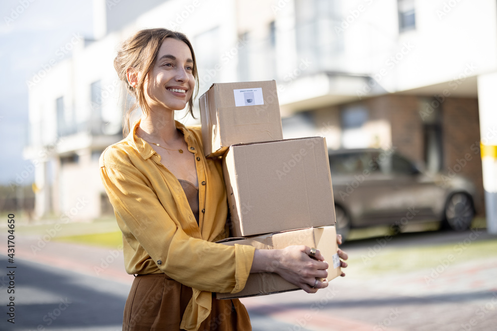 Wall mural young happy woman carries home a parcels with goods purchased online at the modern residential distr