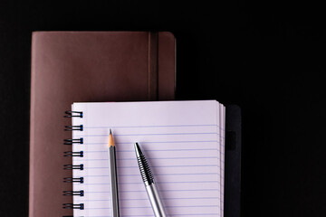 Top close up shot of an opened note book over brown colored diary with pen and pencil put on ruled paper -study notes concept.