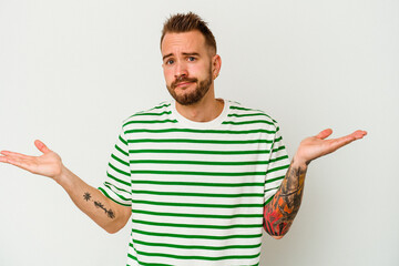 Young tattooed caucasian man isolated on white background confused and doubtful shrugging shoulders...