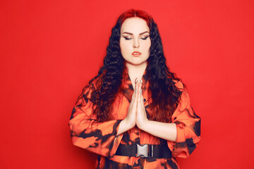 Beautiful girl on a red background. Brunette with red roots of curled hair in a red dress and red...