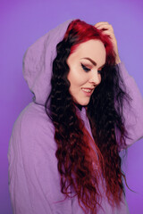 Woman in a blue sweater on a purple background posing. Beautiful brunette with long hair. Eyeliner and trendy makeup.