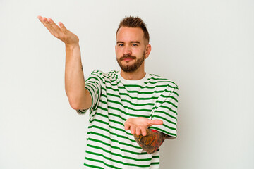 Young tattooed caucasian man isolated on white background makes scale with arms, feels happy and confident.