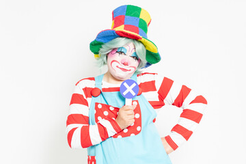 白背景の前に立って、NGのプラカードを持つピエロ