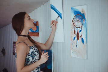Cute girl painting a picture in home studio. Beauty model woman painting her picture. Art. Woman draws paints. Sweet girl engaged in creativity. Model painting brush on easel. Young artist painting .