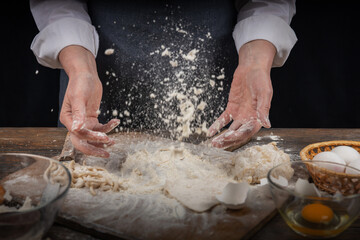 Women's hands, flour and dough. A woman in an apron cooking dough for homemade baking, a rustic home cozy atmosphere, a dark background with unusual lighting.