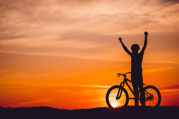 Obraz premium Silhouette of a mountain biker at sunset with arms raised
