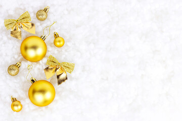 Fototapeta na wymiar Bright golden and yellow Christmas decorations (ribbons, baubles, ornament) on white artificial snow background with copy space. Christmas and New Year traditional holiday celebration concept.