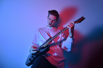 Fototapeta premium Portrait of young man artist singing, screaming, playing electric guitar Hobby, music concept. Rock Star The guy in neon plays the guitar and sings. Music