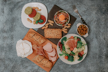 Meat platter and Camembert cheese with baguette. Salad with prosciutto. Olives. Perfect fried eggs with mushrooms and spices. Vegan vegetable cutlets and peanuts. Fork. Food delivery.