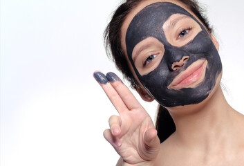 Teenager girl in a black mask, natural photo of a real mask on a young girl. Texture dark cream. Model on a white background smokes skin