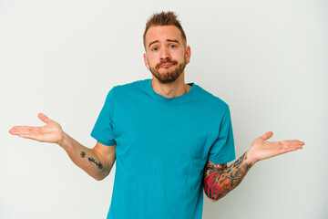 Young tattooed caucasian man isolated on white background doubting and shrugging shoulders in...