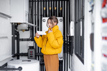 Confused woman looks at electricity bills, comparing data with the meter in the electrical panel at...