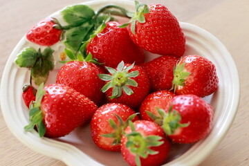 Strawberries  on a white plate against a wooden background.