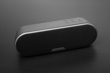 Musical black speaker . Bluetooth technology for playing tracks remotely. On a dark wooden table.