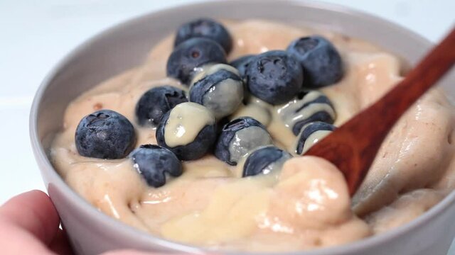 Banana dairy-free ice cream or vegan smoothie bowl with berries and tahini, white table.