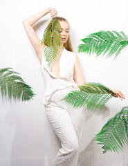 Beautiful girl smiles and laughs, dances in the tropical leaves. Chic white suit. Summer fashion....