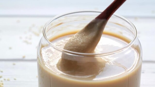 Sesame paste - tahini in a glass jar, stir with a spoon, close-up.