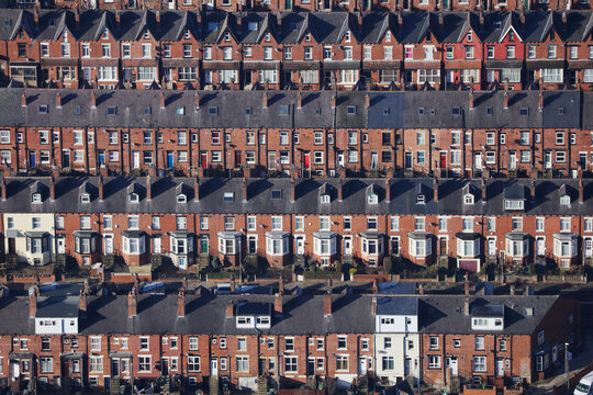 An aerial view taken from a helicopter of suburban terraced streets and roads in Britain. Many brick homes in a row making a striped abstract pattern. A vibrant local community.