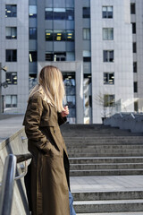Fototapeta premium Woman stands against a business center. Young businessperson near an office building in the financial district of the city. Urban concept. Walk in a modern city.